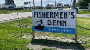 A sign for Fishermen's Denn LLC with a silhouette of a fisherman on a boat. - Fishermen’s Denn, close to Lake Erie Islands, boat ramps, ferries, and marinas (Port Clinton)