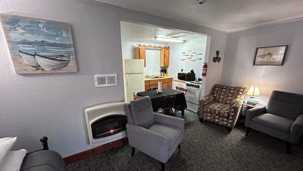 A living room with a fireplace, two armchairs, a patterned sofa, a dining table with chairs, and a kitchen area with a refrigerator, microwave, and stove. - Fishermen’s Denn-Marblehead and Port Clinton  vacation area (Port Clinton)