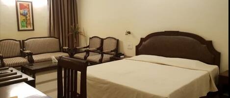 Una habitación de hotel con una cama, dos sillones, un sofá, una mesa y un cuadro en la pared.