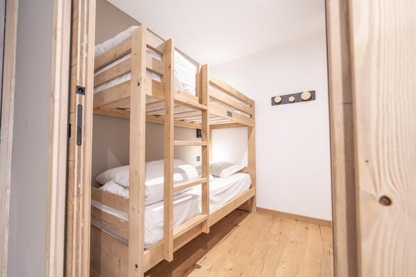 Ein Schlafraum mit Etagenbetten, Holzboden und weißer Bettwäsche.