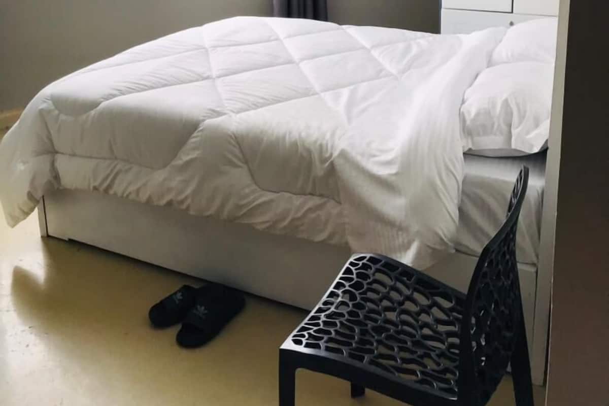 A bedroom with a bed, a chair, a wardrobe, and a window with a view of buildings.