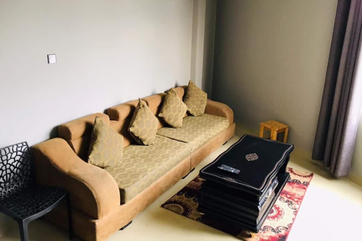 A living room with a sofa, a small wooden stool, and a black metal chair.