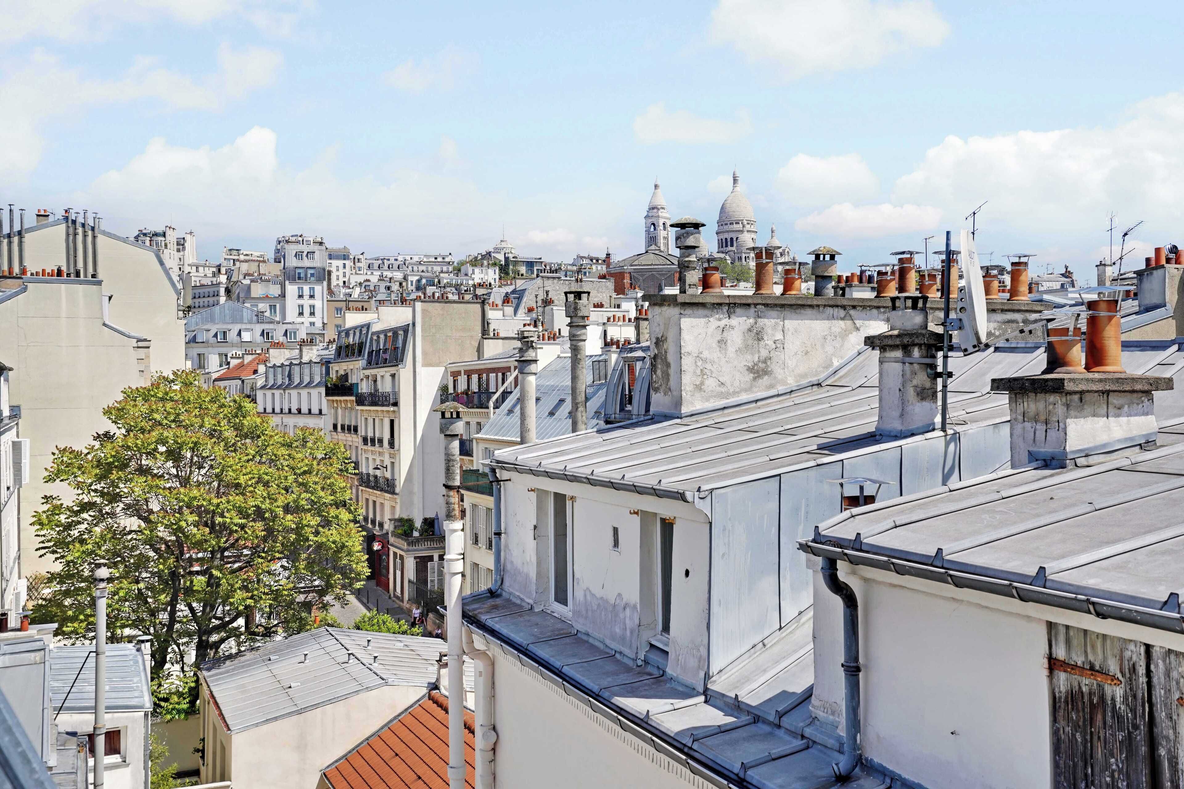 A cityscape with multiple rooftops, including a prominent dome structure and various chimneys.