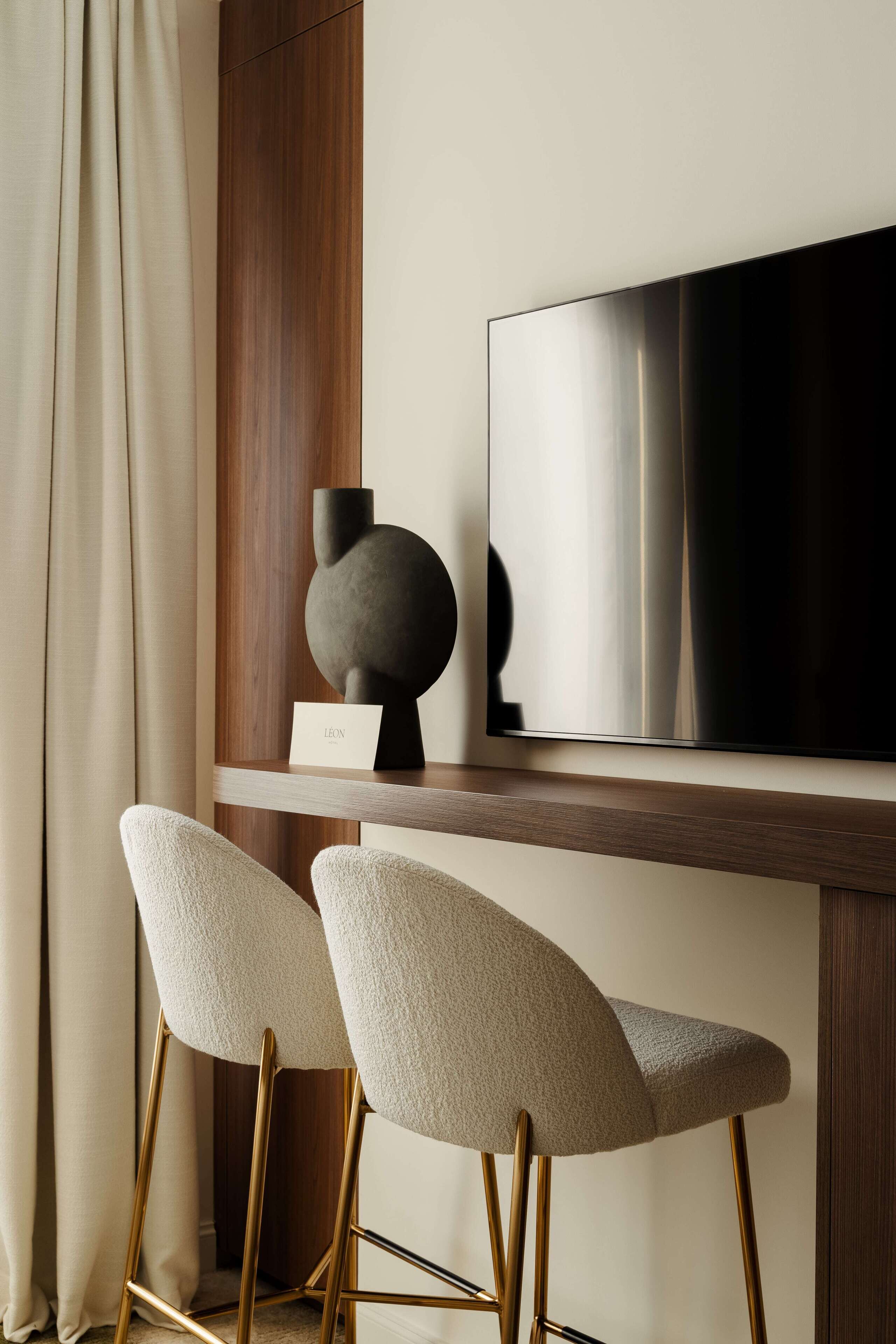 Un espace bar moderne avec deux tabourets hauts, un téléviseur à écran plat et un décor minimaliste comprenant un vase foncé et une plaque nominative.