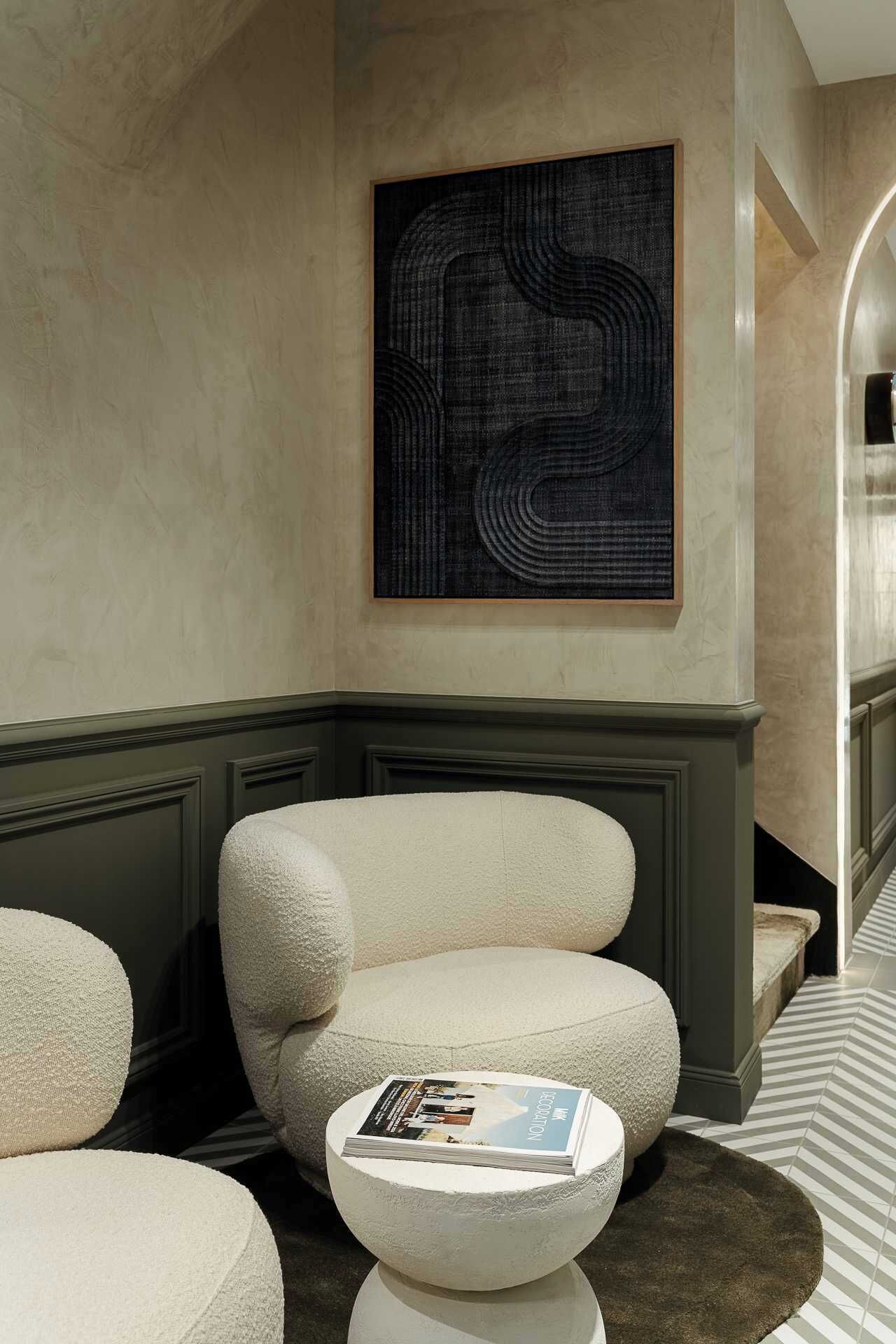 A modern living room with a large abstract painting, a beige armchair, and a round coffee table with a magazine.