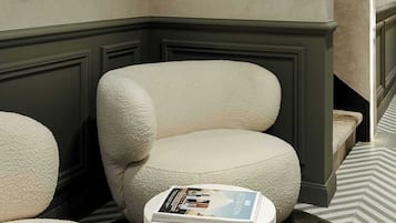 A modern living room with a large abstract painting, a beige armchair, and a round coffee table with a magazine.