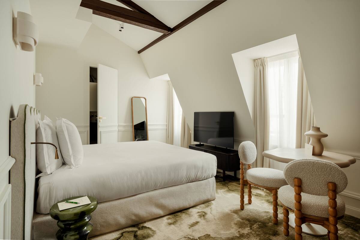 A modern hotel room with a large bed, a TV, a small table, and two chairs.