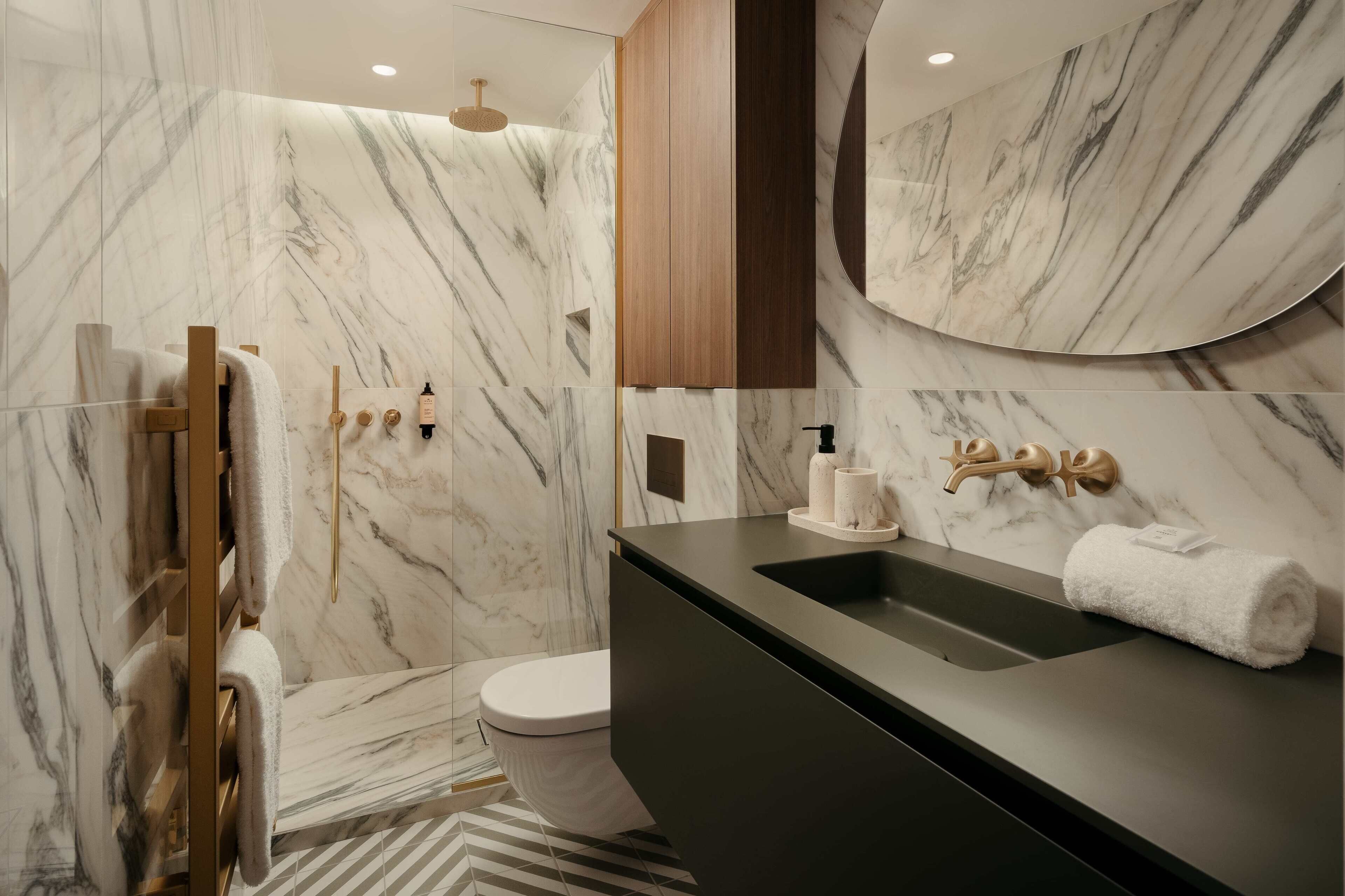 A modern bathroom with marble walls, a wooden vanity, and a shower area.