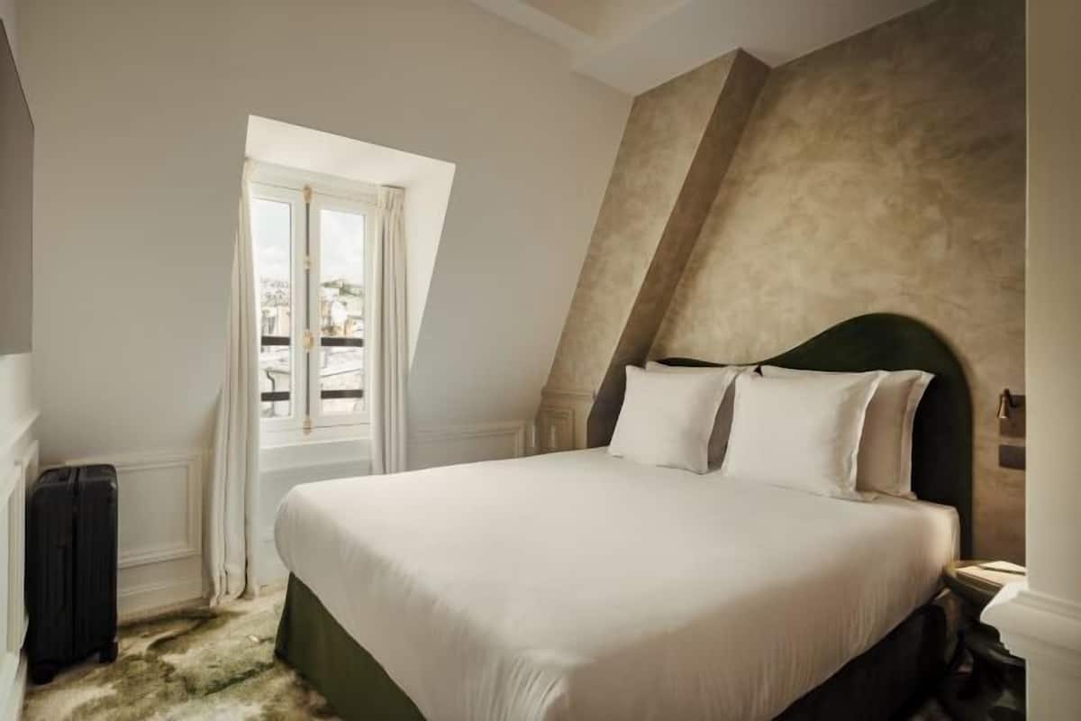 A bedroom with a large bed, a window with curtains, a suitcase, and a textured wall.