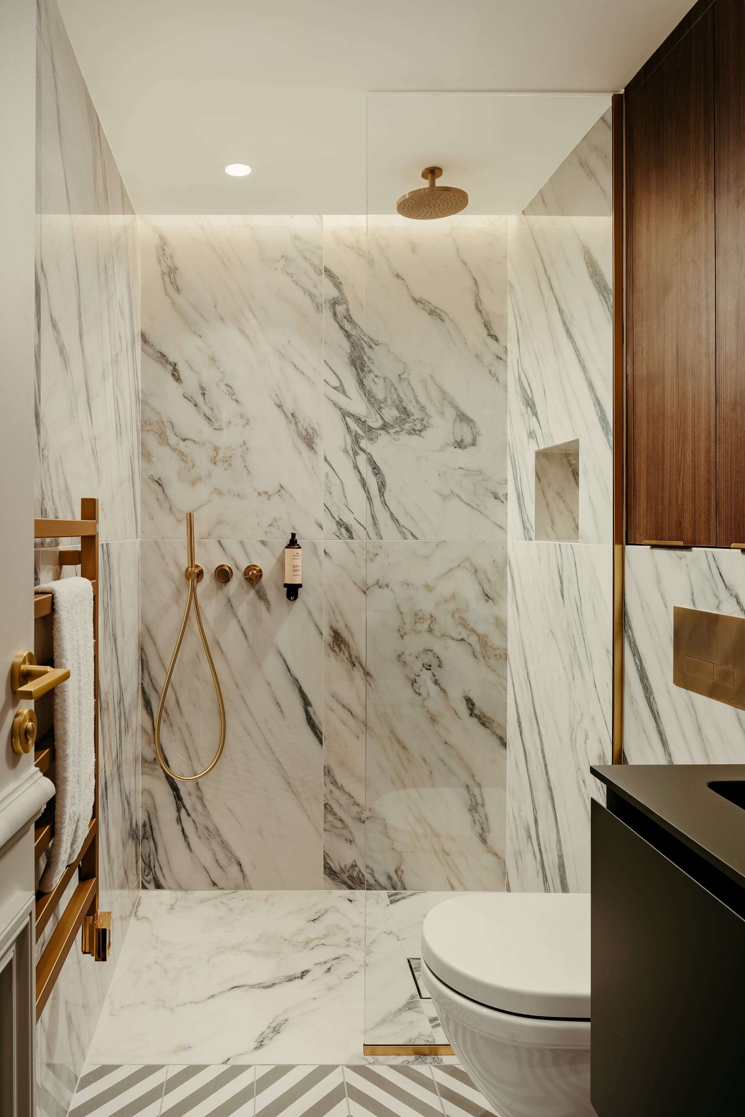 Une salle de bain moderne avec des murs en marbre, une douche dotée de robinetterie dorée et des toilettes.