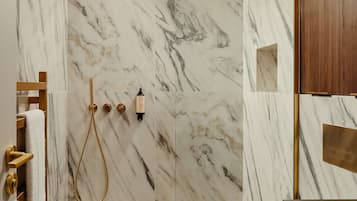 Une salle de bain moderne avec des murs en marbre, une douche dotée de robinetterie dorée et des toilettes.