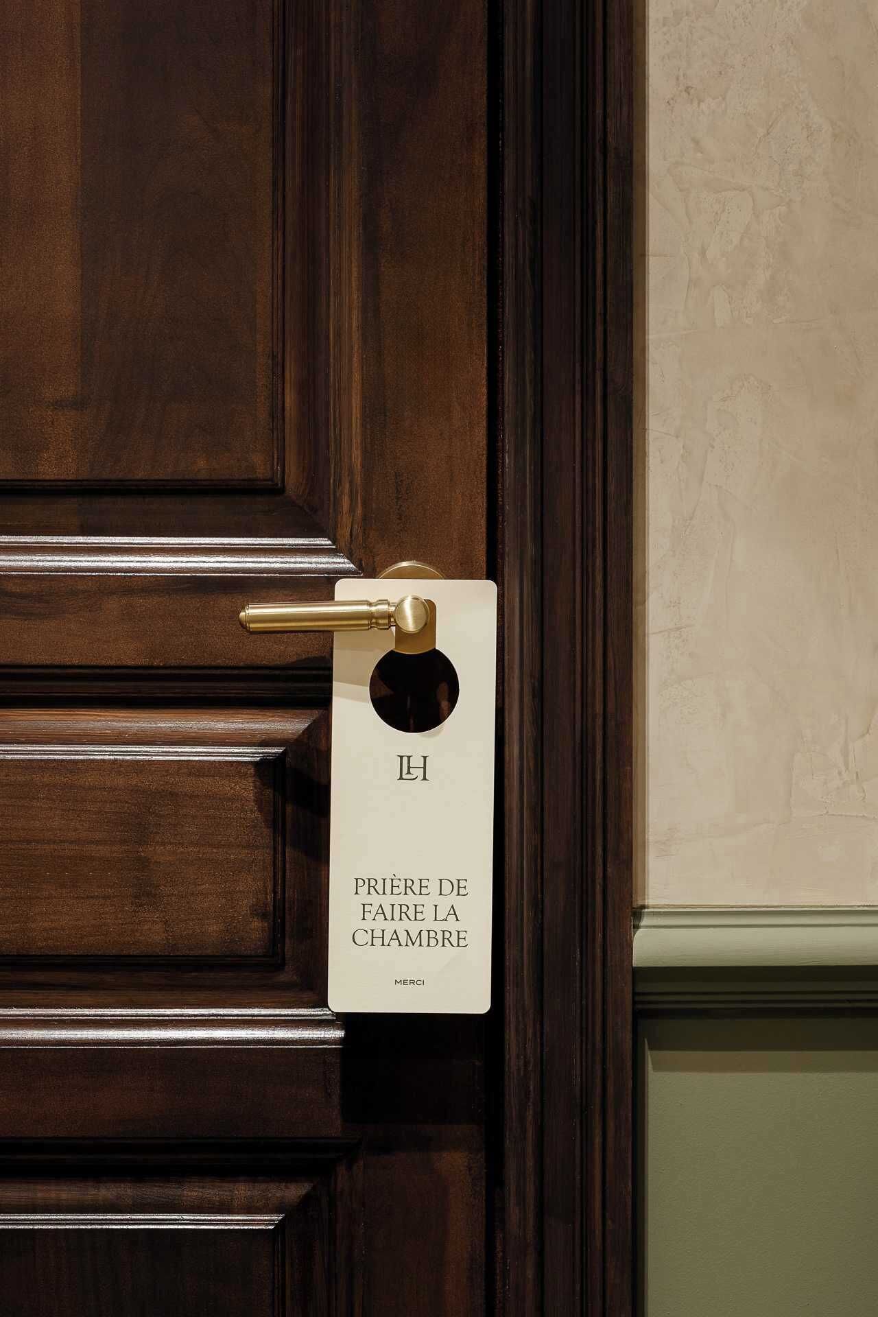 A hotel room door with a brass handle and a sign that reads "PRIERE DE FAIRE LA CHAMBRE" with "MERCI" below it.