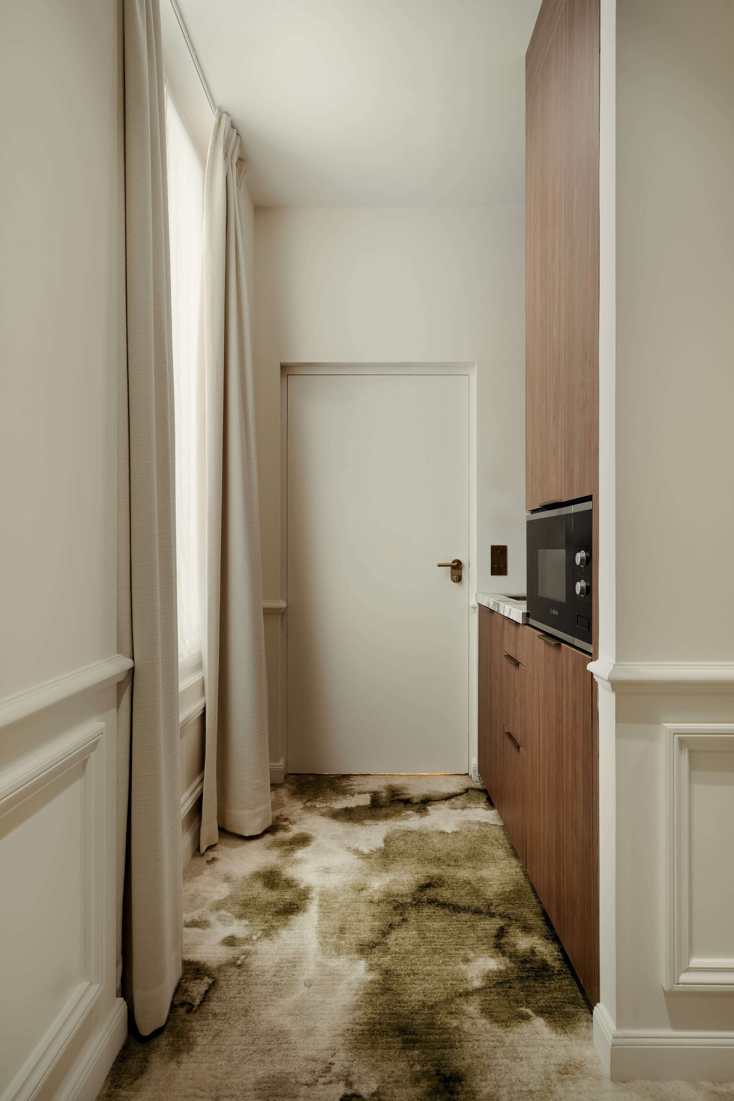 Un couloir étroit avec une porte, un four à micro-ondes posé sur un meuble en bois et un tapis taché.