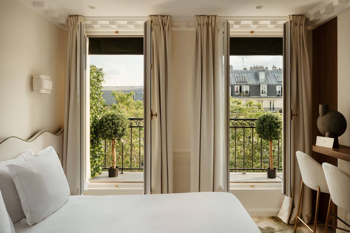 A hotel room with a bed, a chair, a window with curtains, and a view of the outside.