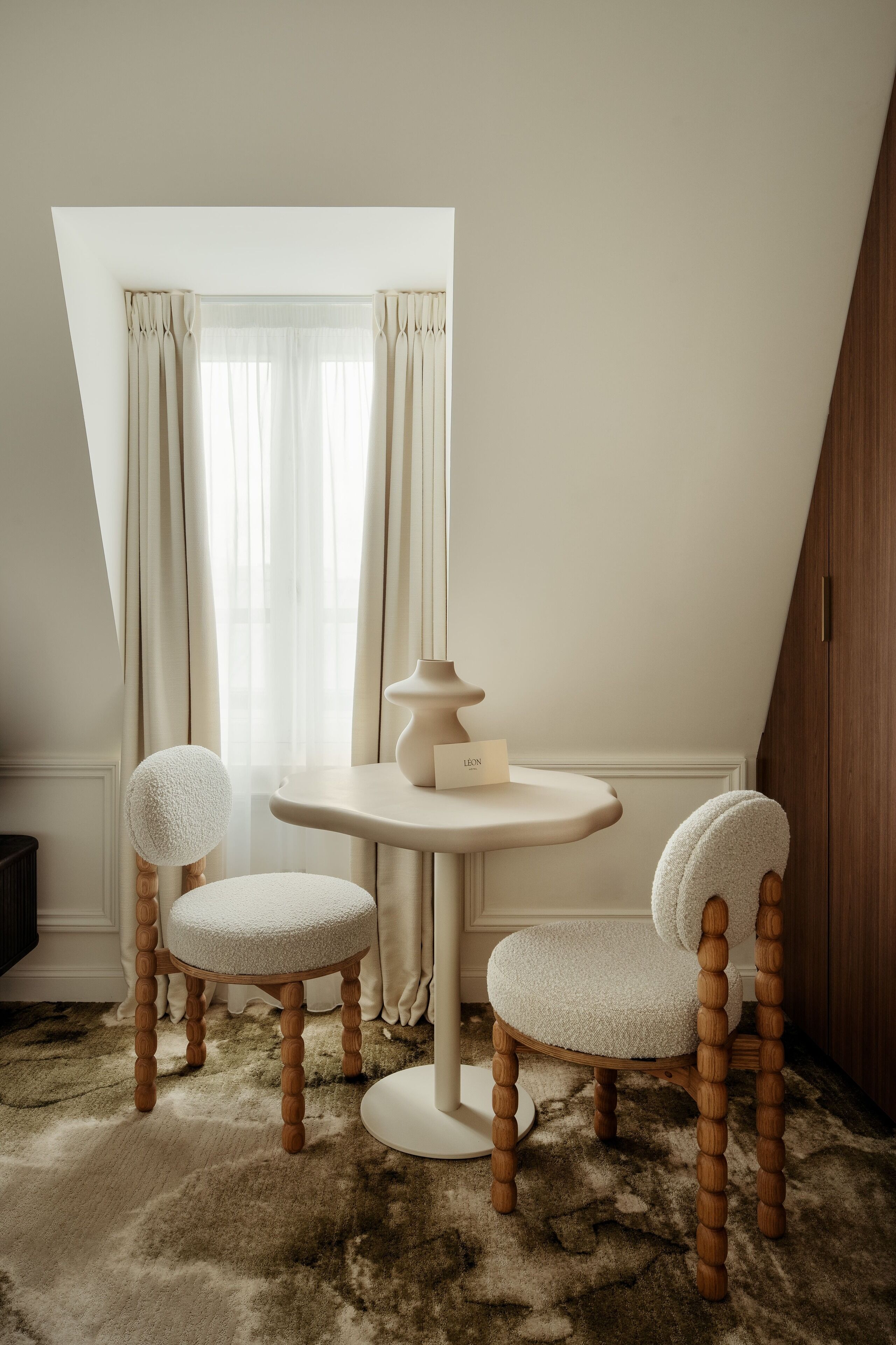A room with a round table, two chairs, a small table with a vase, and a window with curtains.