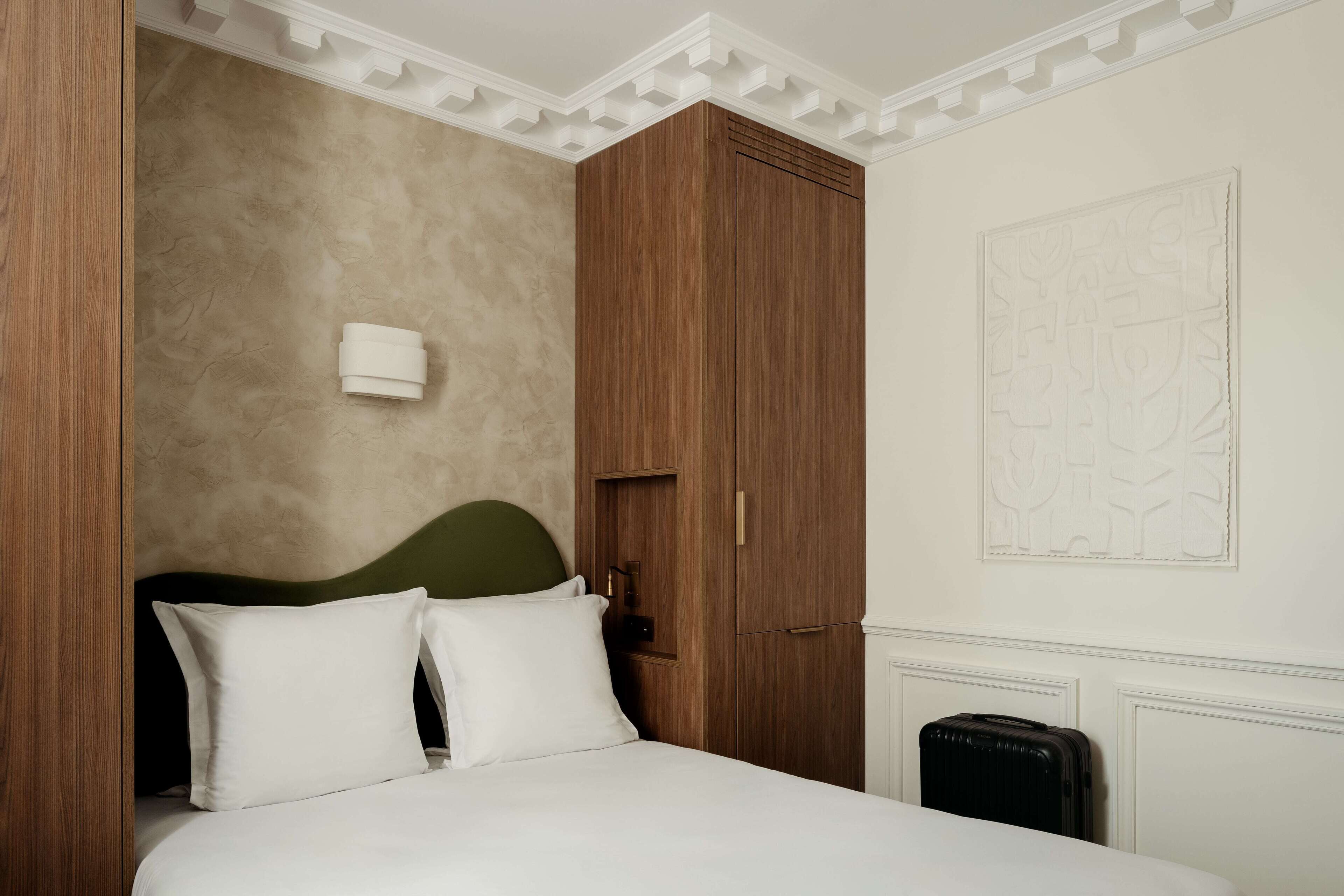 Une chambre à coucher avec un lit, une armoire en bois, une tête de lit verte et un luminaire fixé au mur.