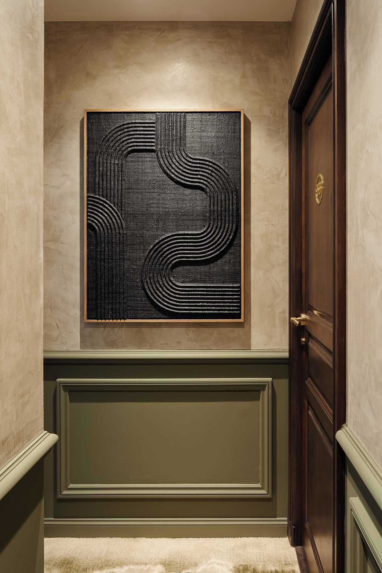 Un couloir orné d’une œuvre d’art abstraite encadrée au mur, une porte en bois et un escalier recouvert de moquette.