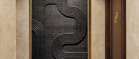 Un pasillo con un cuadro abstracto enmarcado en la pared, una puerta de madera y una escalera con alfombra.