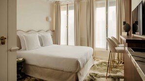 Ein Hotelzimmer mit einem großen Bett, einem Schreibtisch mit Stuhl, einem Fernseher und einem Fenster mit Vorhängen.