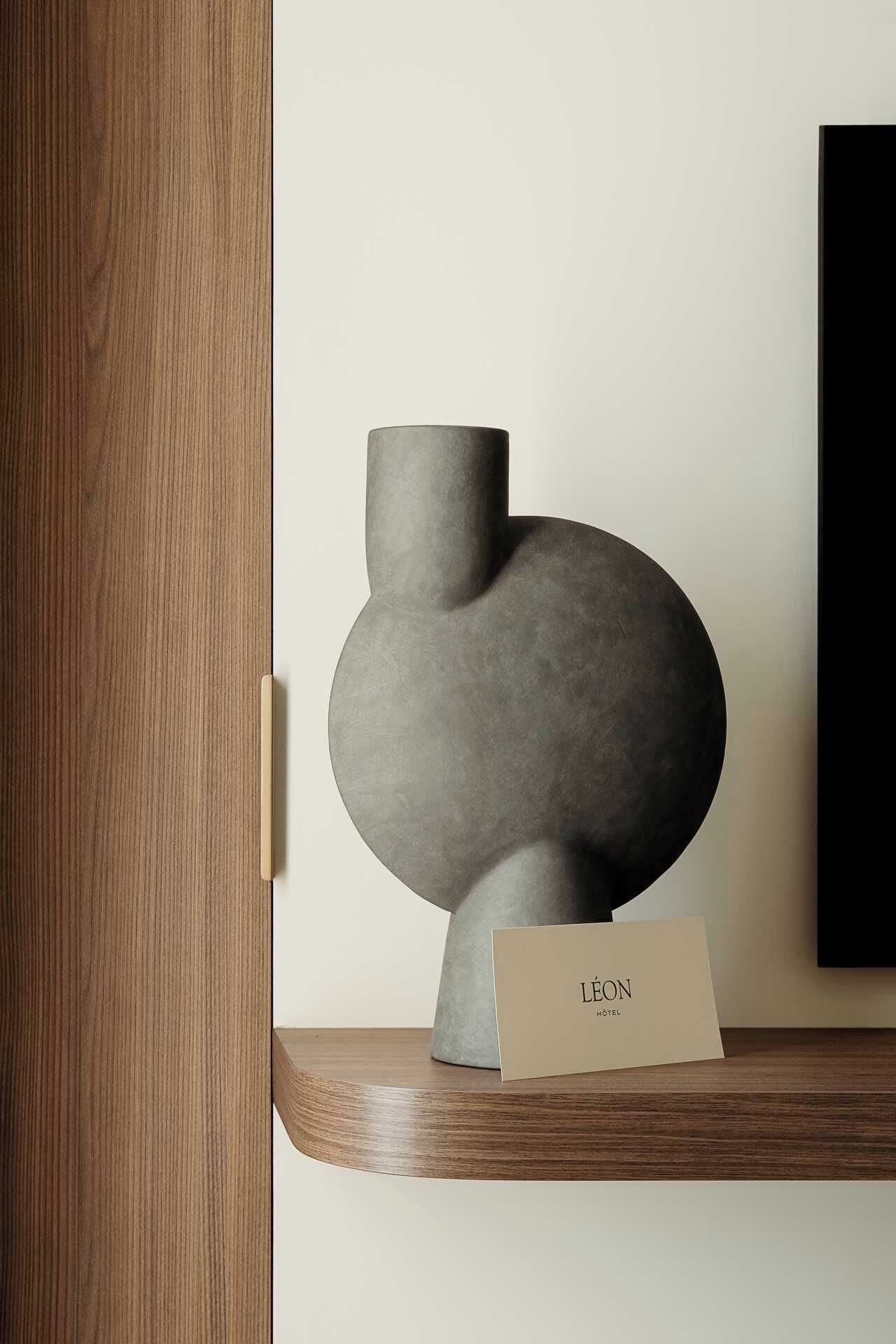 A modern sculpture on a wooden shelf with a card labeled "Léon Hotel".