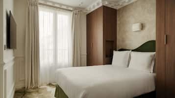 A hotel room with a large bed, wooden wardrobe, a flat-screen TV, and a window with curtains.
