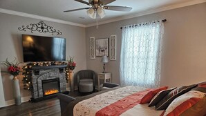 Ein Schlafzimmer mit Kamin, einem Bett mit rot-weiß gestreifter Bettdecke, einem Sessel, einem an der Wand montierten Fernseher und einem Deckenventilator.