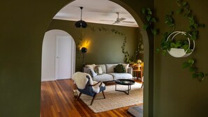 A cozy living room with a sofa, armchair, and coffee table, an arched doorway, and a ceiling fan. - LOLA COTTAGE - MI CASA TU CASA (Kyneton)