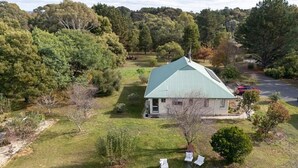 A house with a green roof, surrounded by a well-maintained lawn and trees. - LOLA COTTAGE - MI CASA TU CASA (Kyneton)