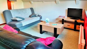 Un salon moderne avec un canapé gris, un divan en cuir noir, une table basse en bois, un téléviseur posé sur un meuble en bois et une lampe fixée au mur.