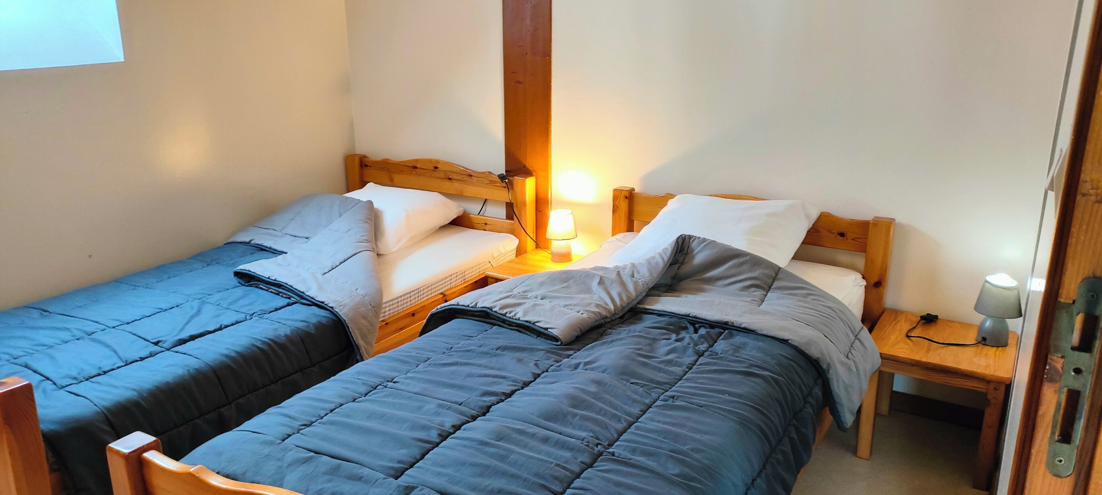Ein Zimmer mit zwei Einzelbetten, jeweils mit einem Holz-Kopfteil, einem Nachttisch mit Lampe und einem kleinen Tisch ebenfalls mit Lampe.