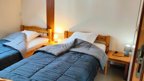 Une chambre avec deux lits simples, chacun doté d’une tête de lit en bois, d’une table de chevet avec une lampe et d’une petite table également équipée d’une lampe.