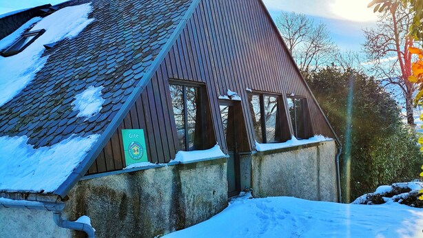 Un bâtiment doté d’un toit en pente recouvert de neige, d’une gouttière bien visible et d’une enseigne sur laquelle on peut lire le mot « Gîte ».