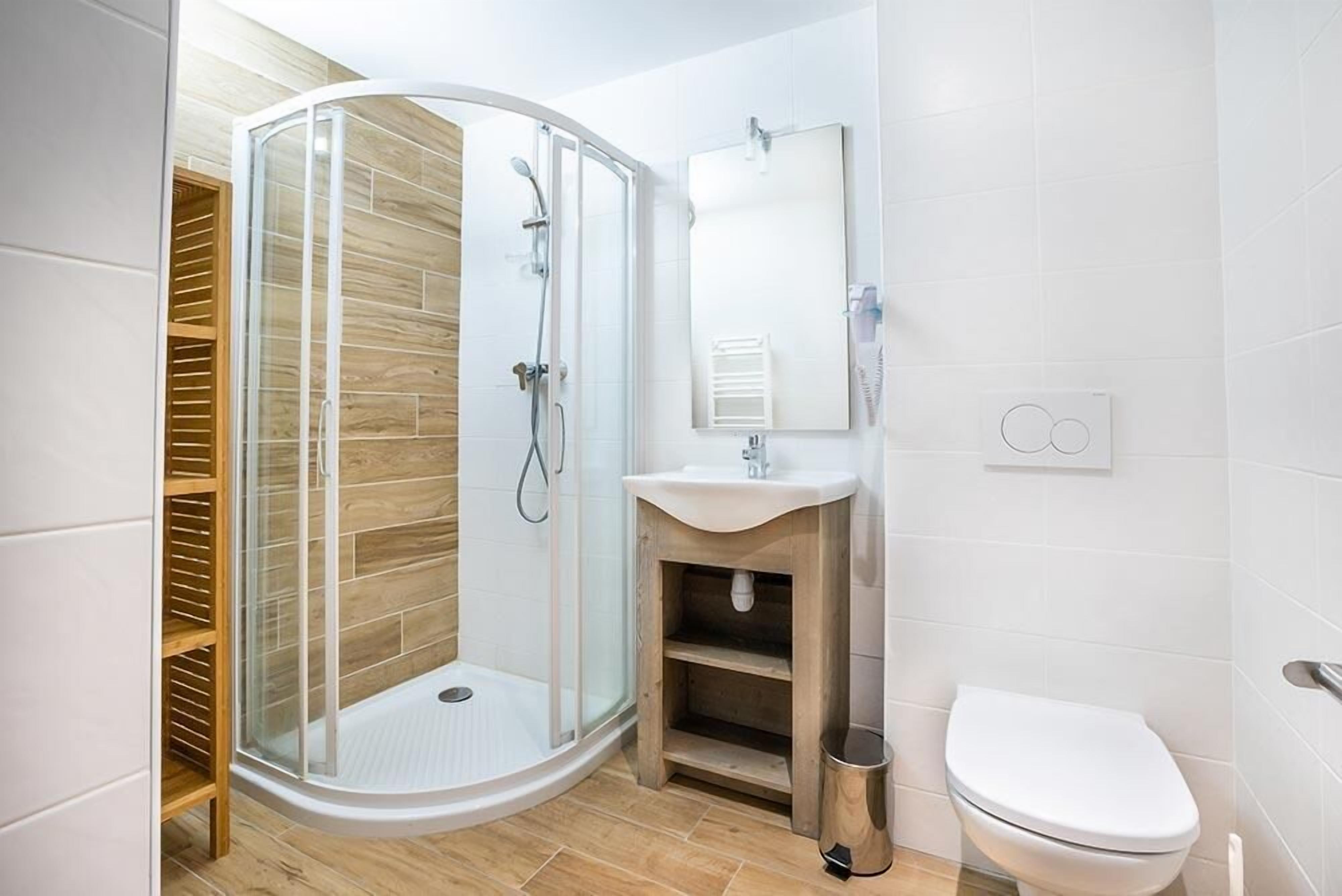 A modern bathroom with a glass-enclosed shower, a wooden vanity, a white sink, and a toilet.