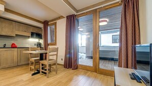 Una cocina moderna con armarios de madera, una mesa de comedor y sillas. Hay una puerta corrediza de vidrio que da a un balcón.