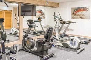 Ein Fitnessraum mit Cardiogeräten, einem Fernseher und Kunstwerken an den Wänden.