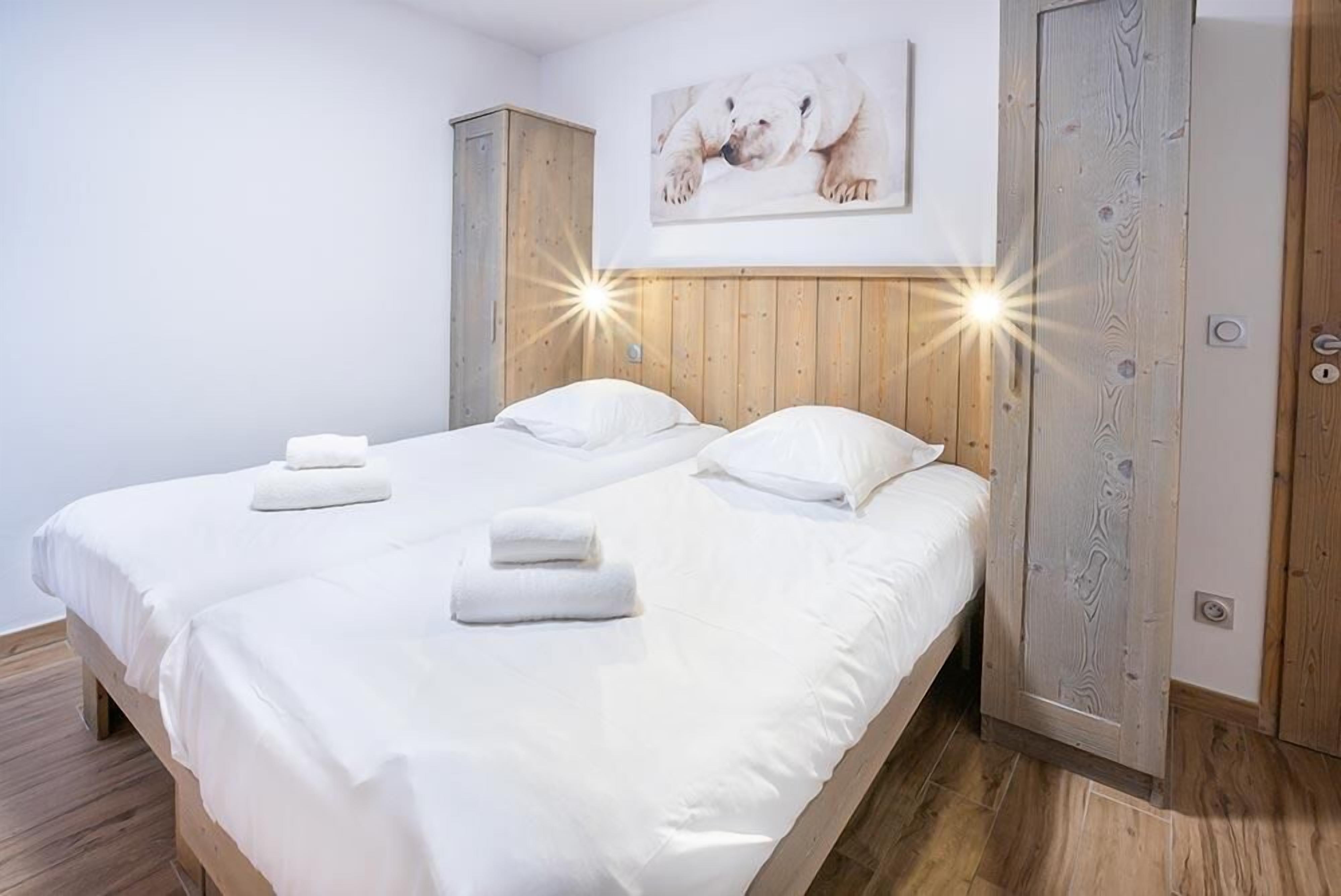 Un lit double avec du linge de lit et des serviettes blanches, une tête de lit en bois et une œuvre d’art représentant un ours polaire accrochée au mur.