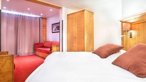 A bedroom with a large bed, wooden wardrobe, and a red chair.