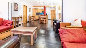 A spacious living area with a wooden table, red sofas, and a kitchen in the background.