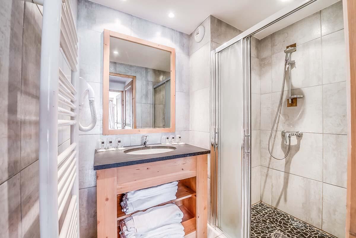 A modern bathroom with a wooden vanity, a large mirror, a sink, and a walk-in shower.