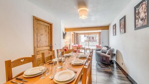 Un coin repas avec une longue table en bois, dressée pour quatre personnes, des chaises et une vue sur la rue.