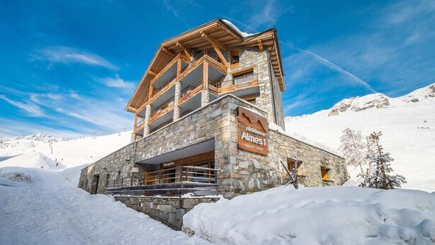 Un bâtiment en pierre doté d’un balcon en bois, portant l’inscription « Residencia Almes 1 », se dressant sur fond de montagnes enneigées.
