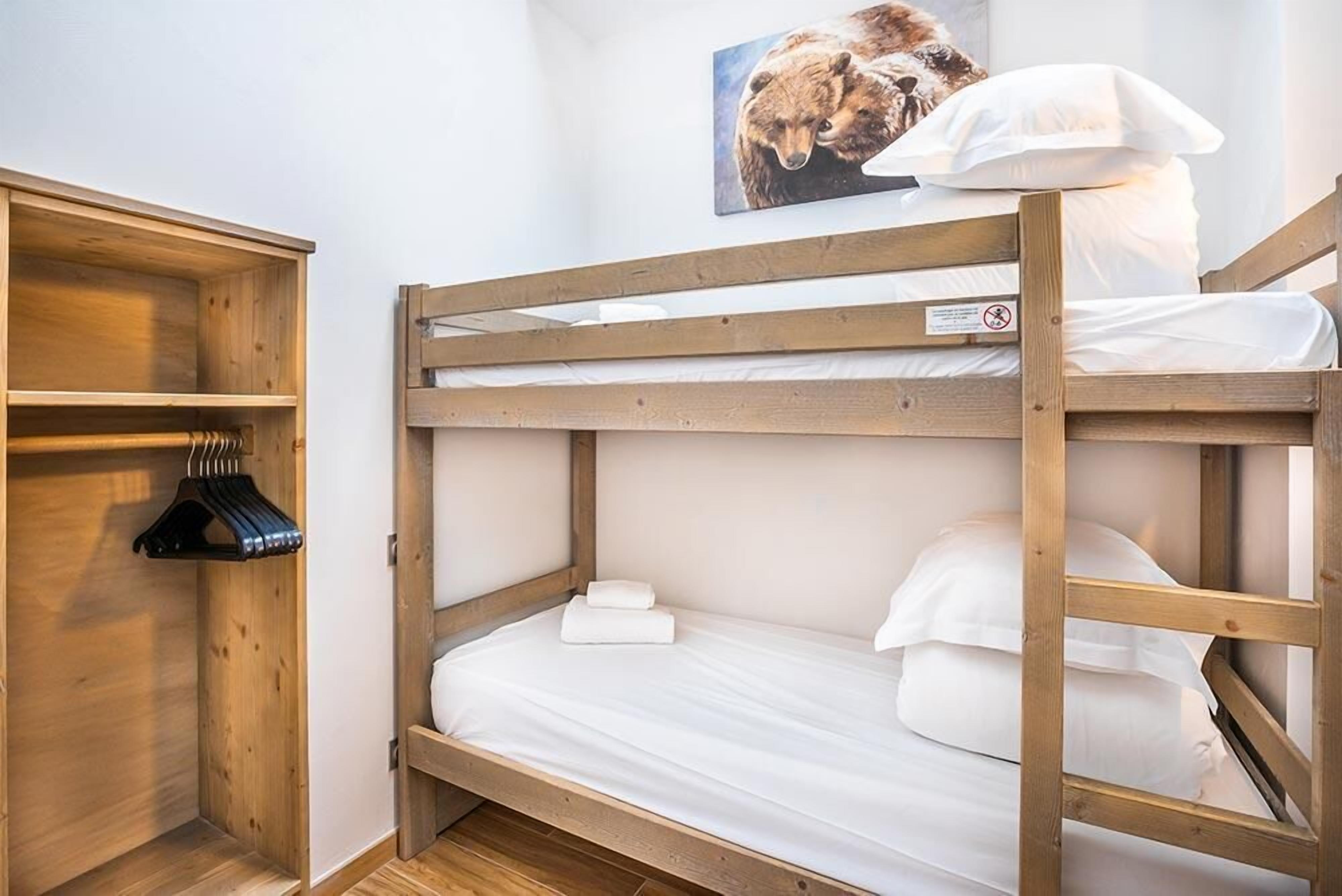 Un lit superposé avec une structure en bois, un portant à vêtements suspendu et un tableau accroché au mur.