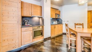 A modern kitchen with wooden cabinets, a microwave, and a dining area with a table and chairs. - Wifi, 2nd floor, terrace, tv, ski locker, 59m², Tignes (Tignes)