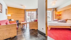 A cozy room with a wooden ceiling, a bed with a red bedspread, a wooden sofa, a small table, and a chair. - Wifi, 2nd floor, terrace, tv, ski locker, 59m², Tignes (Tignes)