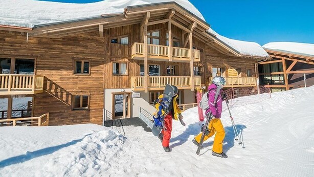 Een houten chalet met balkon en een skilift op de achtergrond.