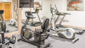 Une salle de sport équipée d’appareils de cardio, d’un téléviseur et d’œuvres d’art aux murs.