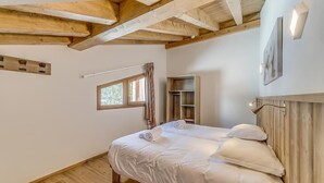Une chambre avec un plafond en bois, un lit avec une literie blanche, une fenêtre avec des rideaux et une étagère intégrée.