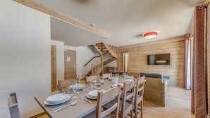 Un coin repas avec une table en bois dressée pour six personnes, un escalier et un téléviseur fixé au mur.
