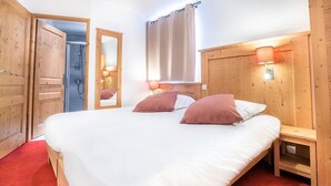 A bedroom with a large bed, wooden headboard, two bedside tables, a mirror, and a shower area. - Wifi, ski-in/ski-out & foot of the slopes, 2nd floor, terrace, tv, ski locker, 65m², Tignes (Tignes)