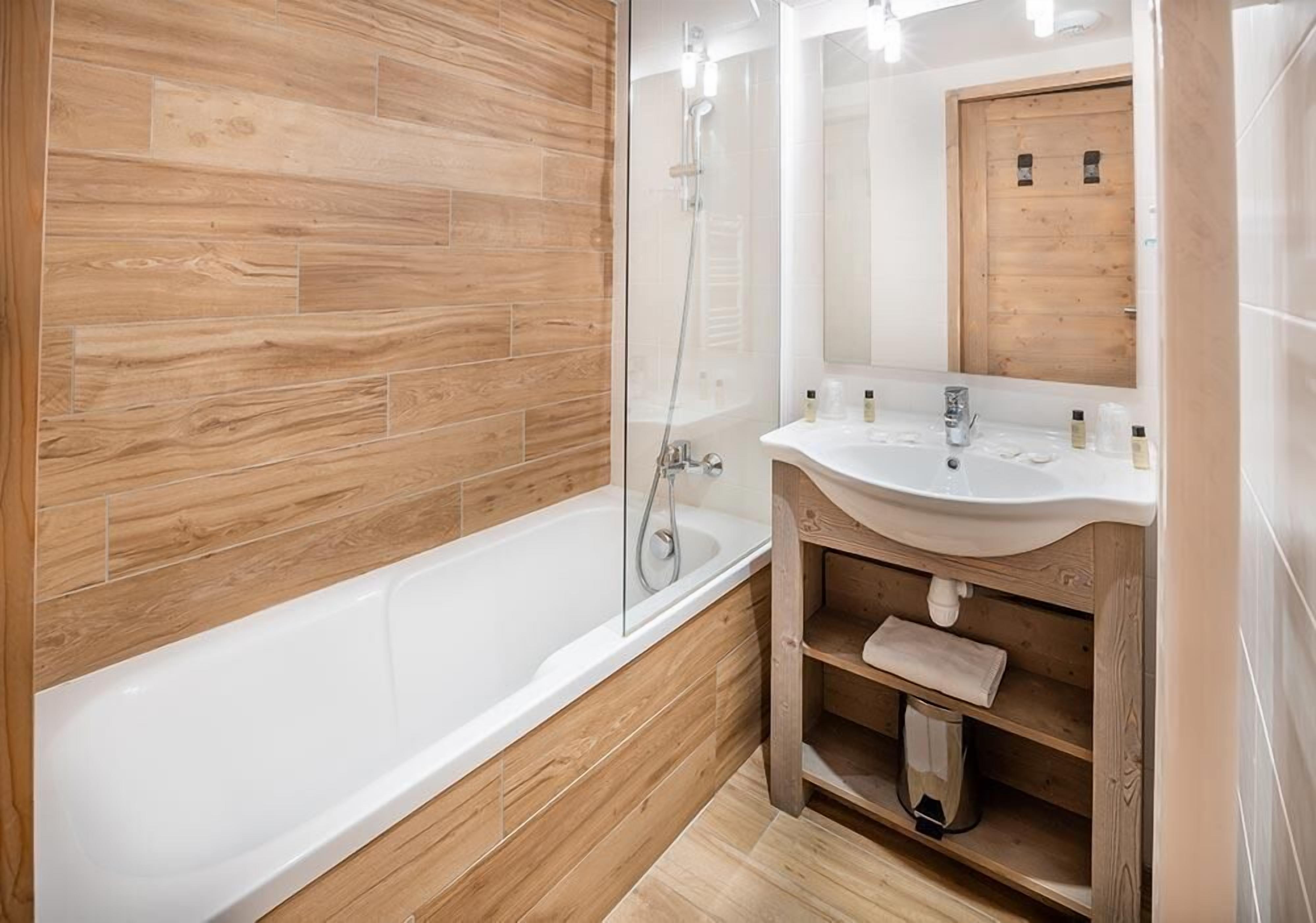 Une salle de bain moderne avec un plancher en bois, une baignoire blanche, un meuble-lavabo en bois et un miroir.
